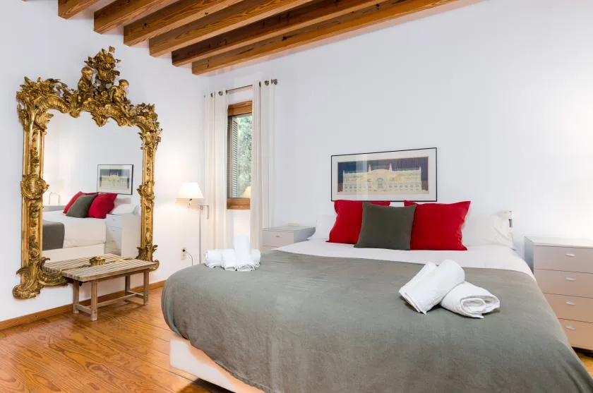 Un dormitorio con una cama vestida con ropa de cama gris y cojines rojos bajo vigas de madera.