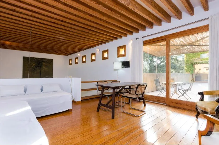 Una luminosa sala de estar con asientos blancos, una mesa de comedor y puertas de cristal.