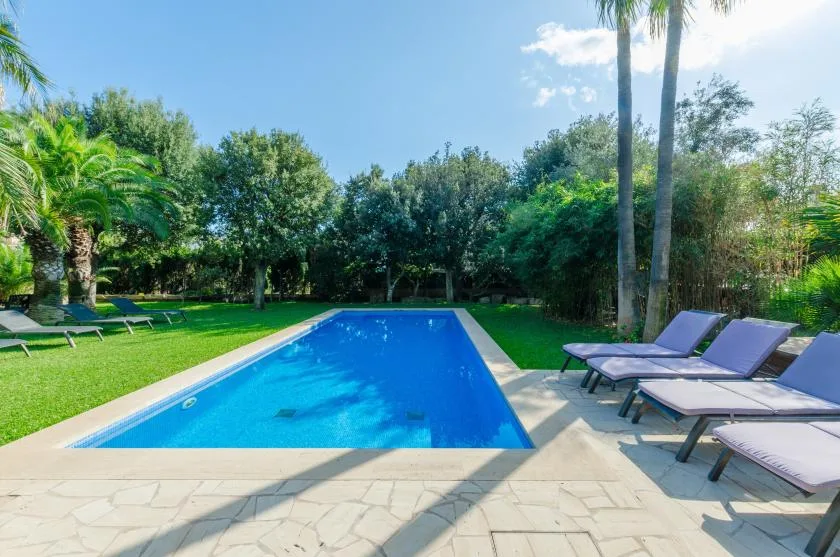 Una piscina al aire libre está rodeada de césped y asientos reclinables.