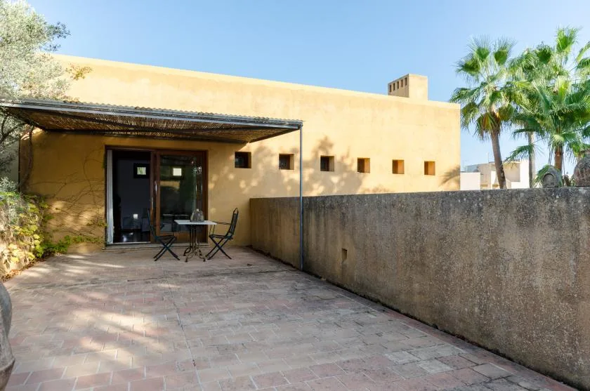 Un patio exterior pavimentado con una zona de estar sombreada junto a un edificio amarillo.
