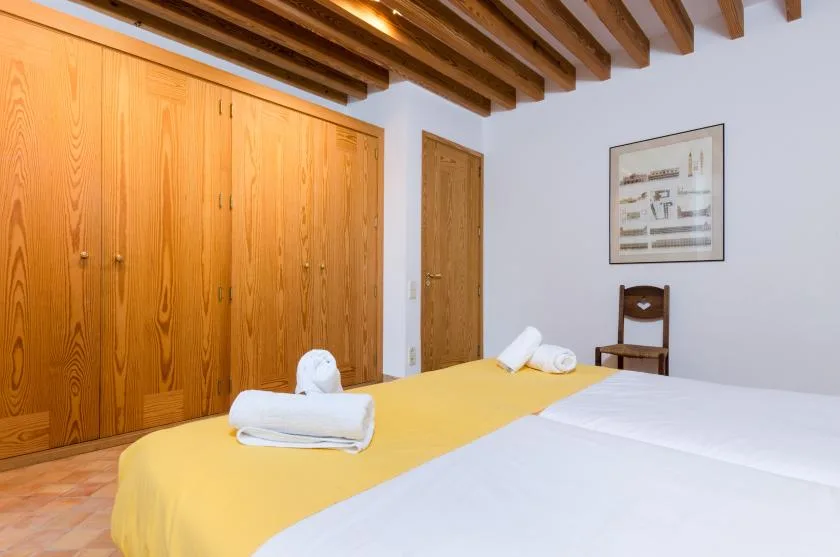 Un dormitorio con dos camas, toallas dobladas, armarios de madera y vigas de techo a la vista.