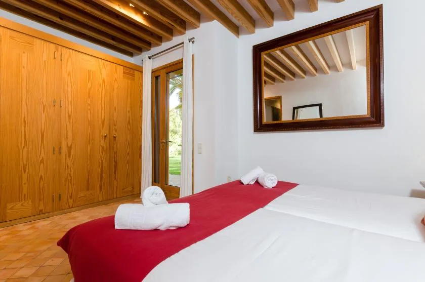 Un dormitorio con ropa de cama blanca y una manta roja bajo vigas de madera expuestas.