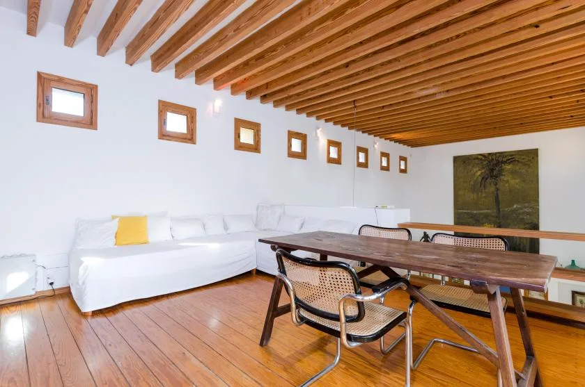 Una luminosa sala de estar y comedor con un largo asiento blanco y una mesa de madera.