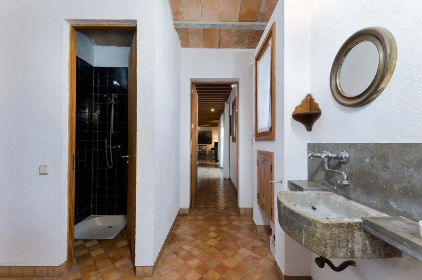 Un pasillo interior estrecho con suelo de baldosas y un lavabo de piedra junto a una puerta.