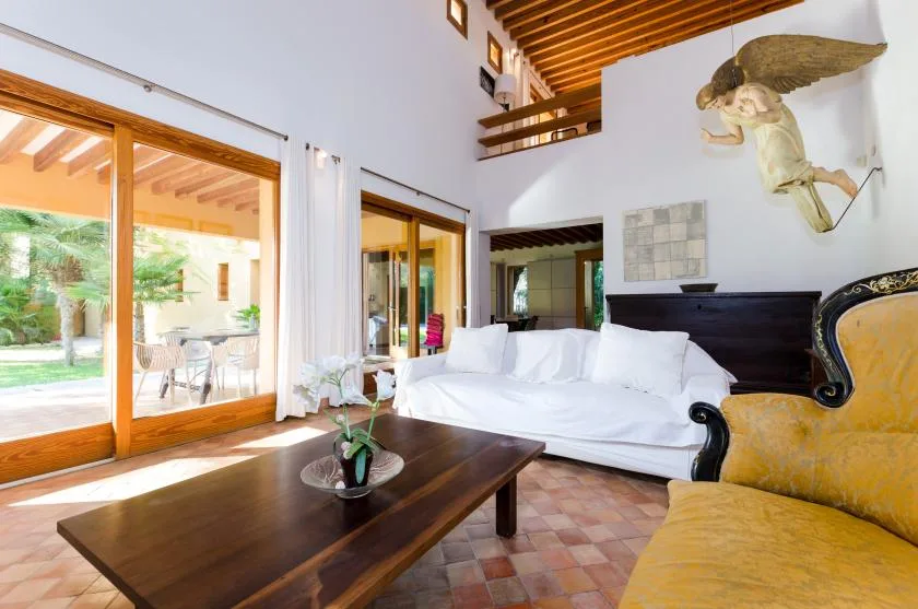 Una sala luminosa con asientos blancos junto a grandes puertas de vidrio que dan a un jardín.