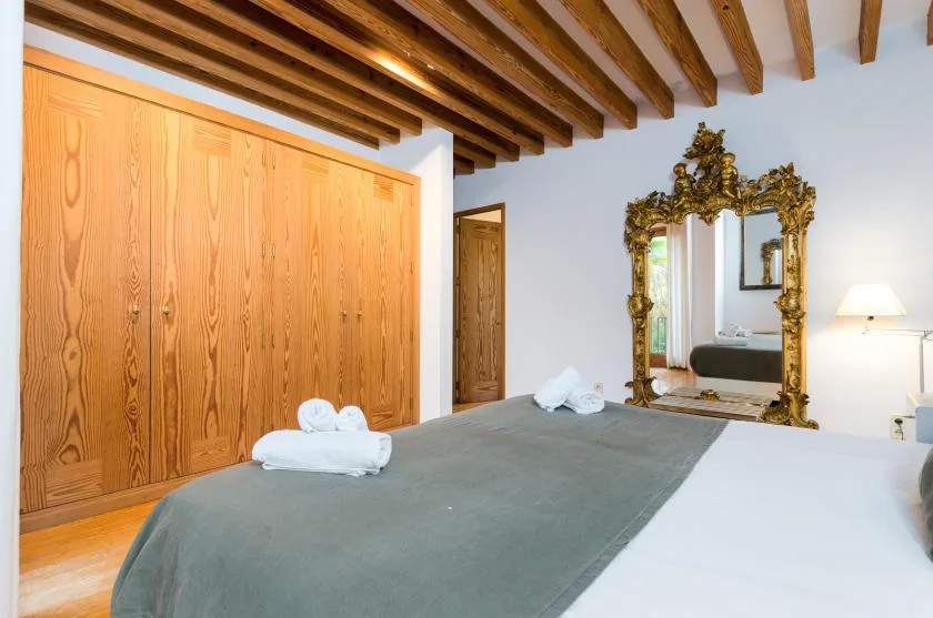 Un dormitorio con una cama arreglada, armarios de madera y un espejo ornamentado.