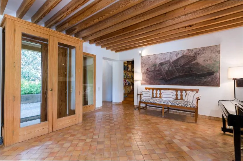 Una sala de estar con vigas de madera en el techo y asientos bajo una obra de gran tamaño.