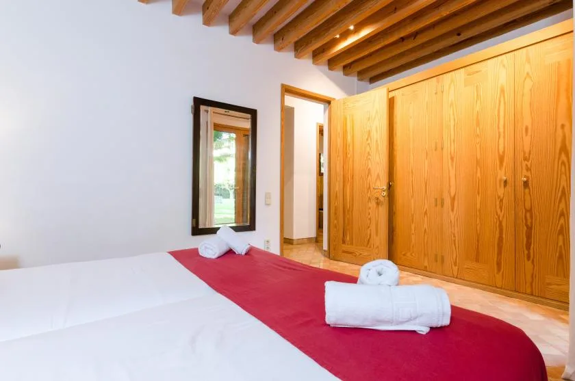 Un dormitorio con ropa de cama blanca, una manta roja y armarios de madera.