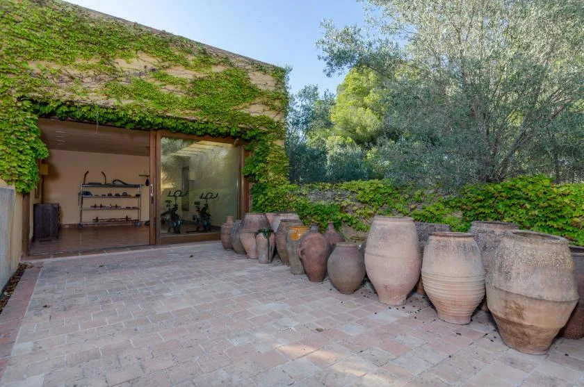 Un edificio cubierto de enredaderas da a un patio pavimentado junto a grandes vasijas.