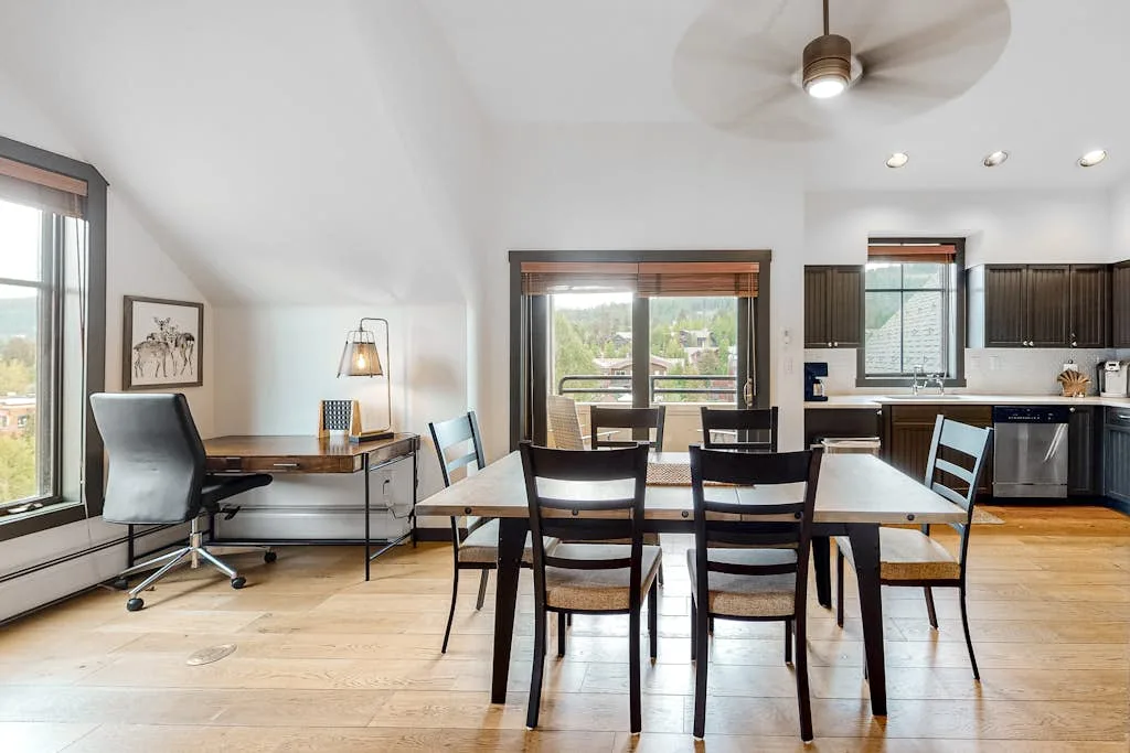 A dining area with a table and chairs beside a kitchen and desk.
