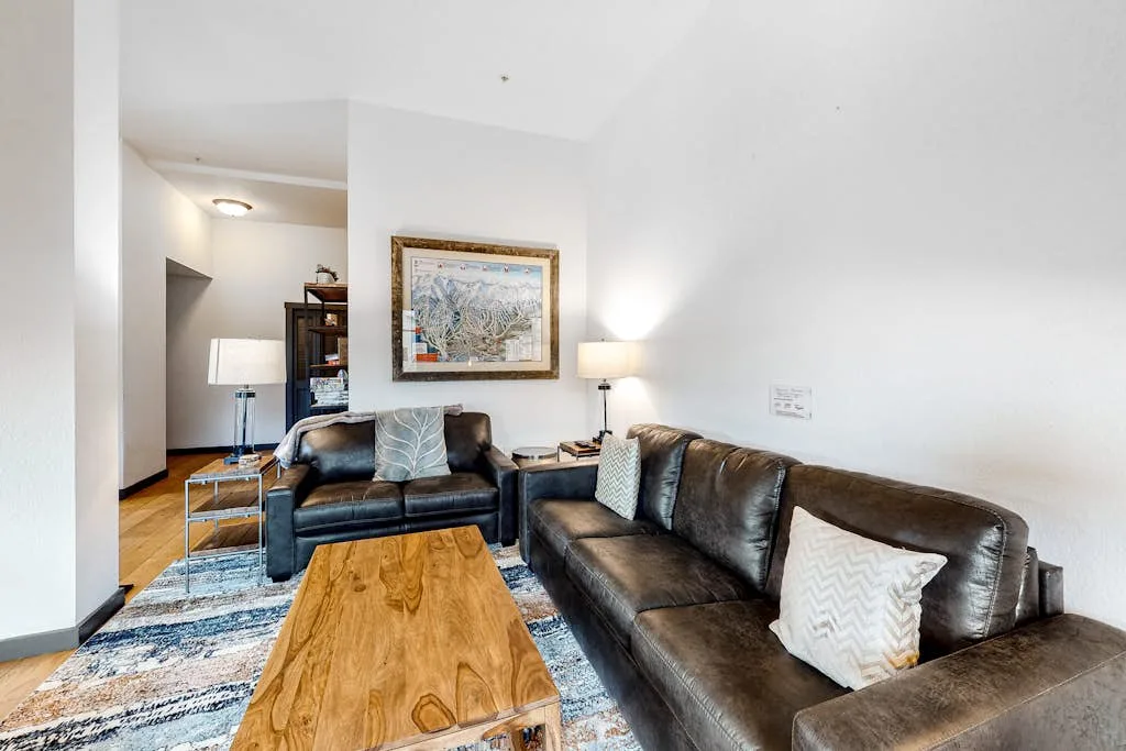 A living room with dark leather seating, a wooden coffee table, and framed artwork.