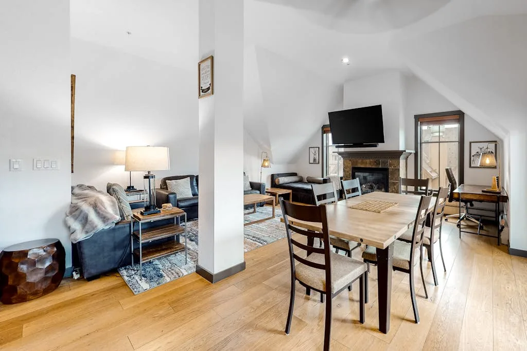 An open living and dining area with a wooden table and seating beside a fireplace.