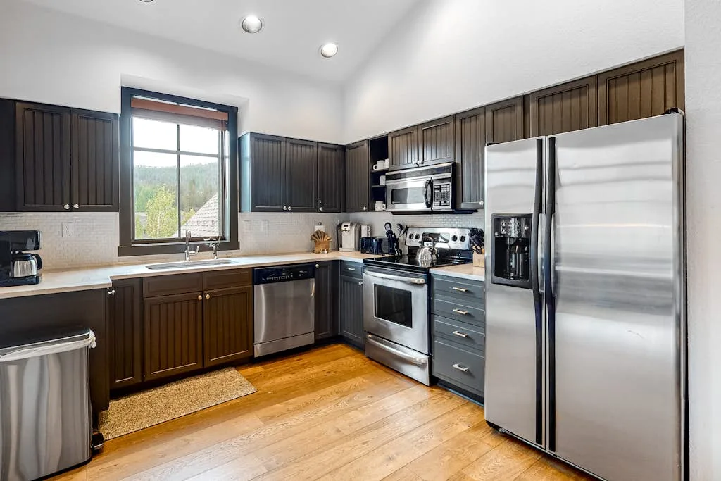 A kitchen with dark cabinets, stainless steel appliances, and wood flooring.