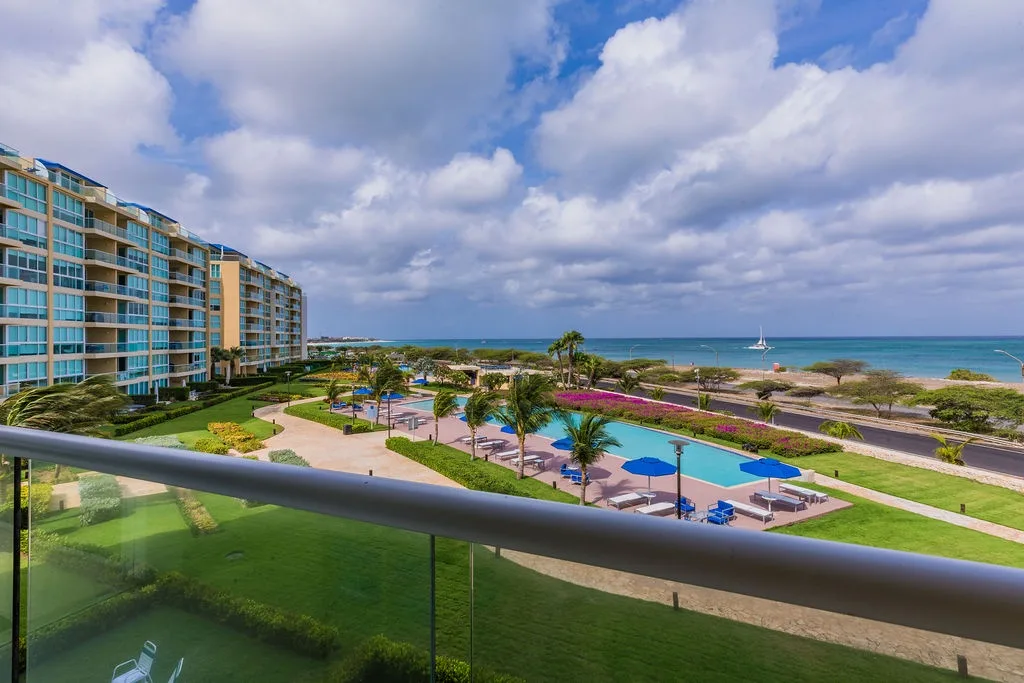 A stunning beachfront resort with lush gardens, sparkling pools, and direct ocean access, framed by dramatic skies and coastal scenery perfect for a tropical getaway.