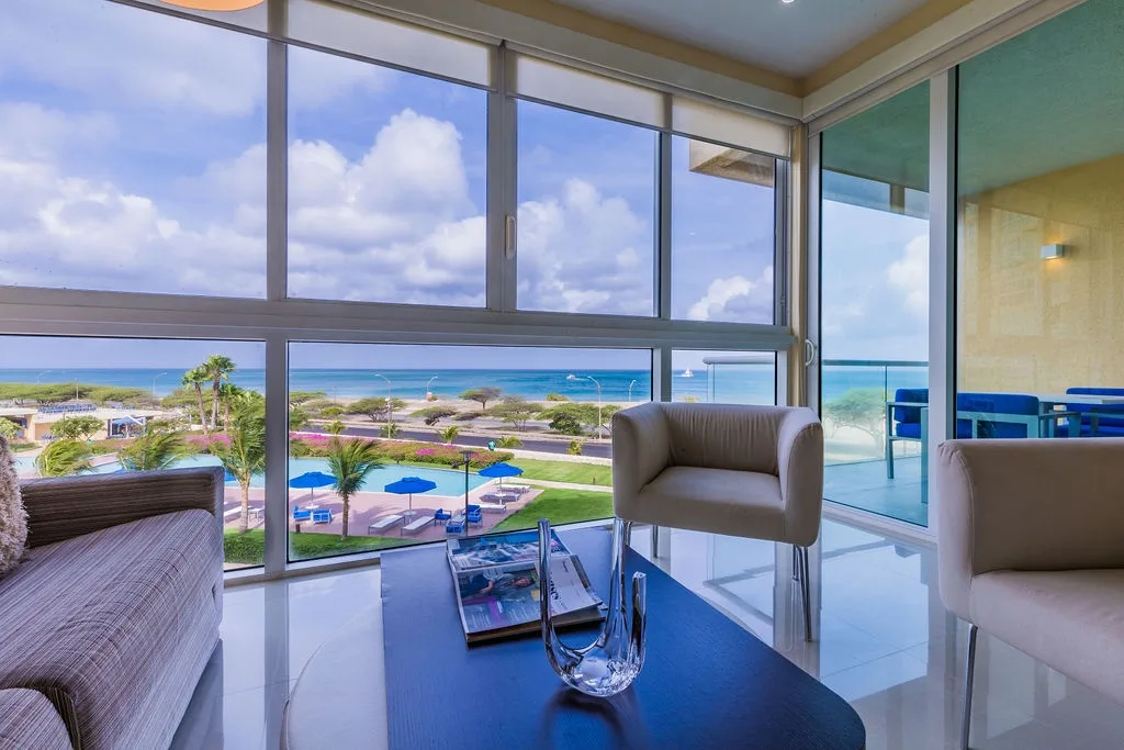 Relax in your stylish living space with breathtaking ocean and garden views through floor-to-ceiling windows, where turquoise waters and tropical palms create your perfect island escape.