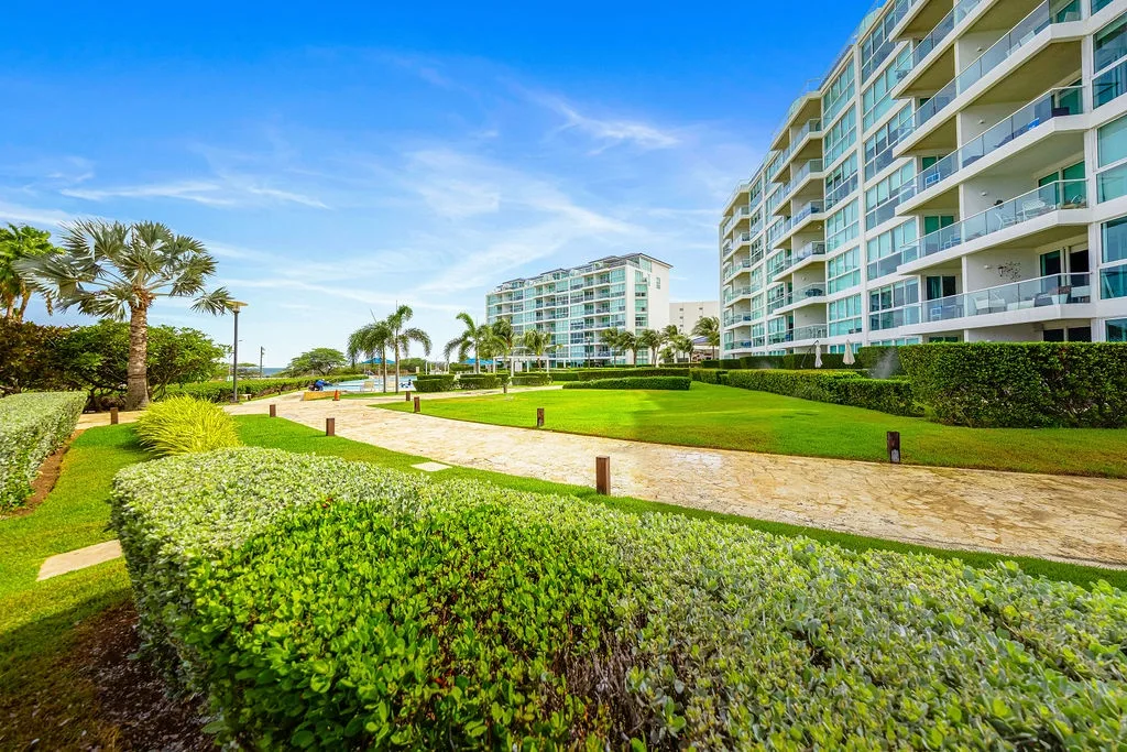 Modern beachfront resort with tropical landscaping and palm trees under clear blue skies.