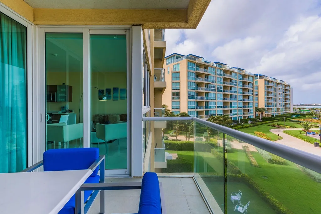 Balcony seating area overlooks landscaped gardens and neighboring resort buildings. Contemporary furnishings provide a comfortable spot to enjoy fresh air and green views from your private outdoor space.