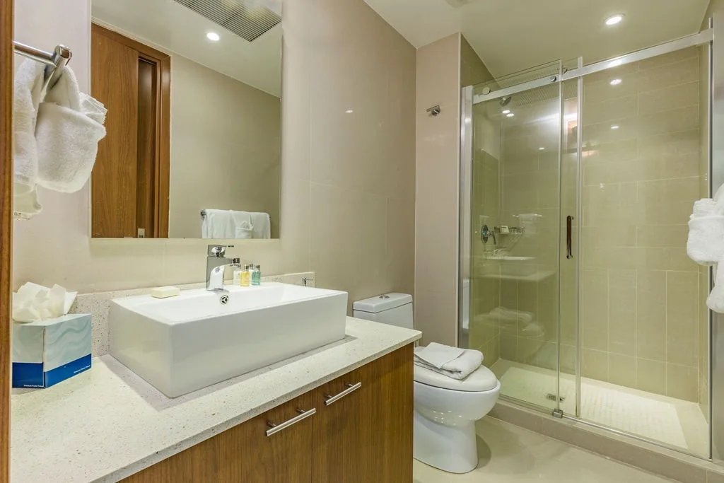 Your private bathroom features a modern vessel sink, generous counter space, sleek glass-enclosed shower, and plush towels ready for your arrival.