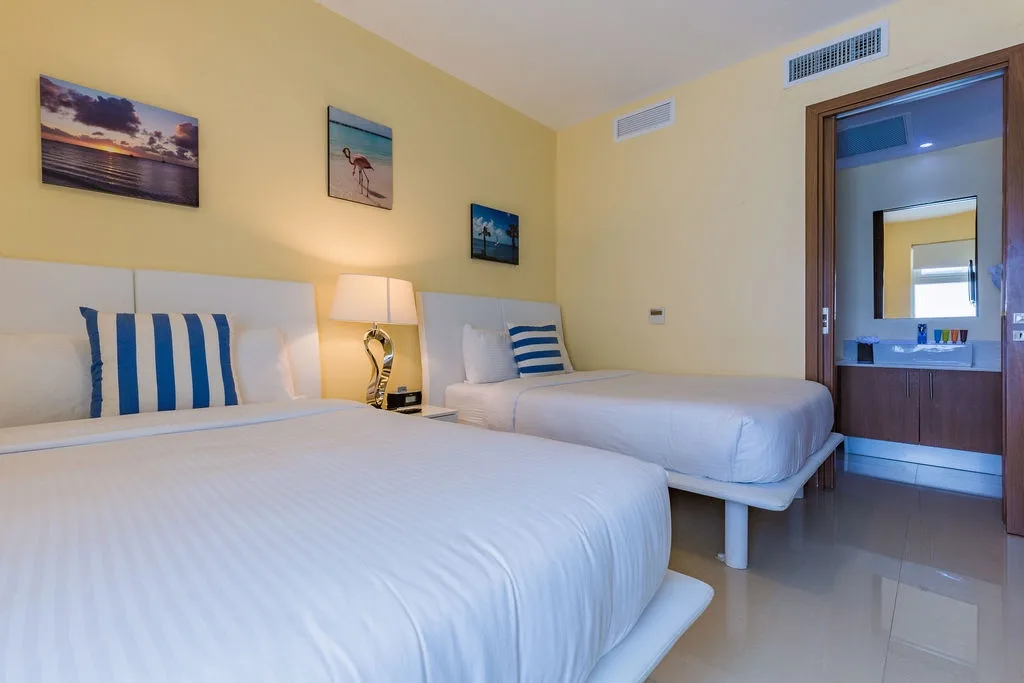 Relax in crisp linens and coastal charm—two plush beds await with beach-themed accents, soft lighting, and a private en-suite just steps away.