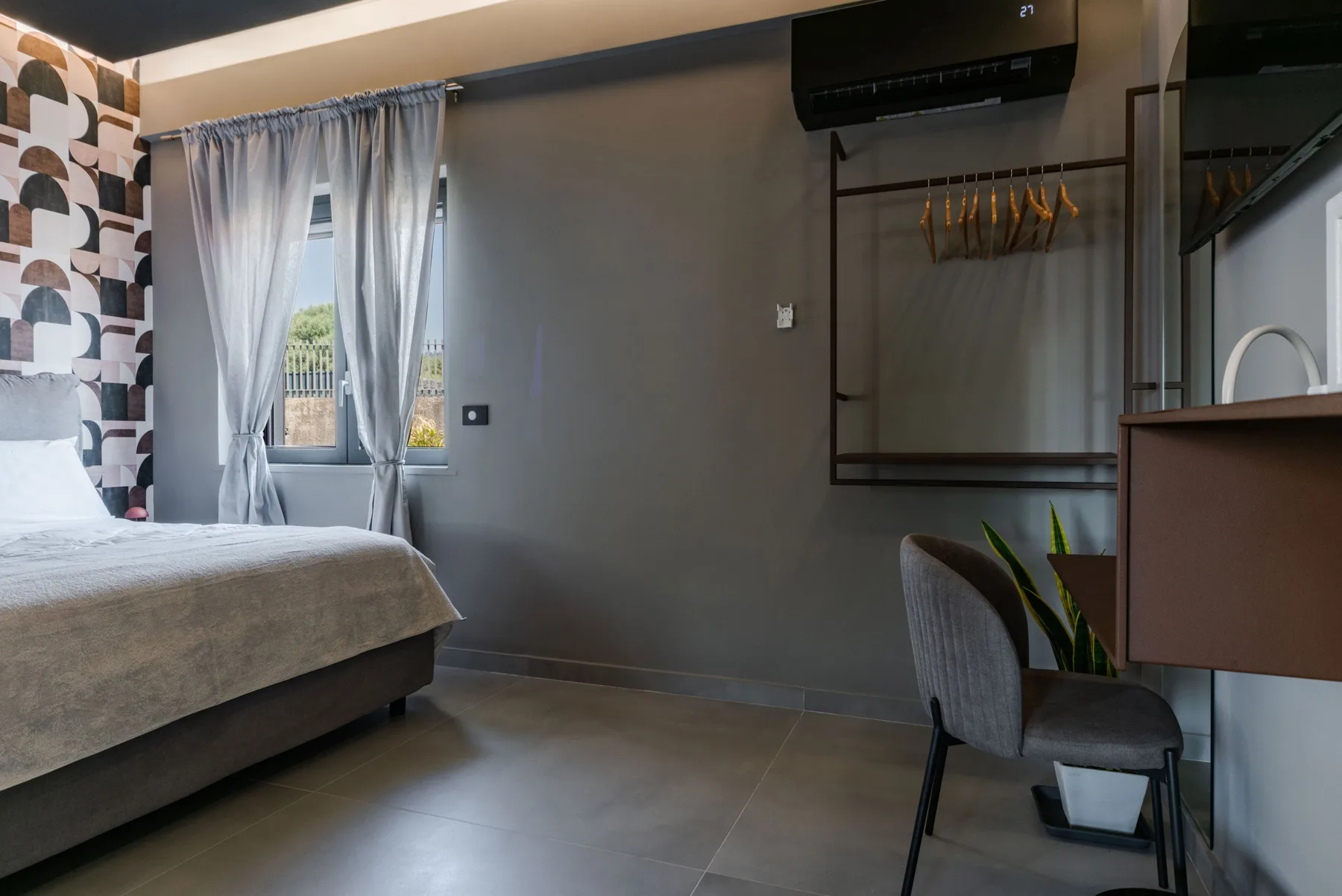A bedroom with a bed, a curtained window, and a small desk area.