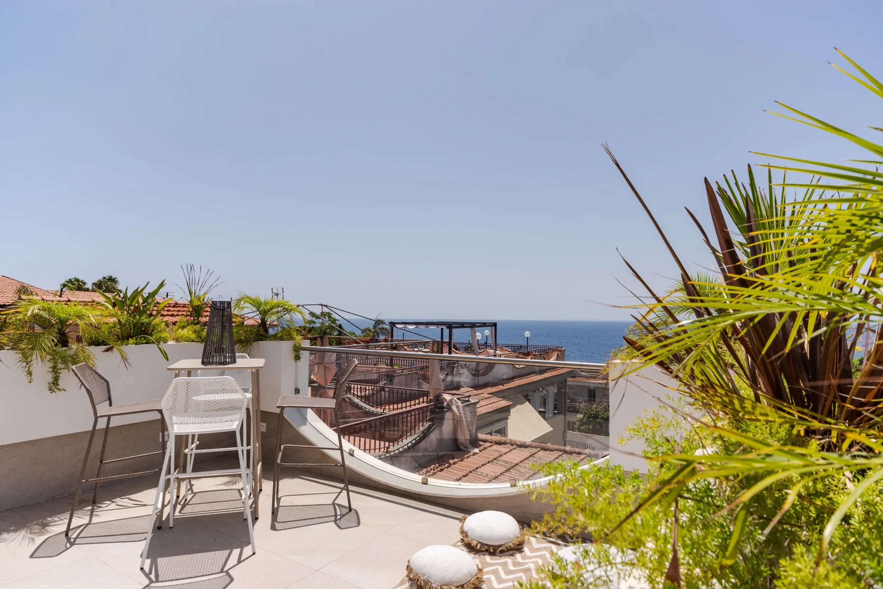 A sunny terrace with seating and a view of the sea.