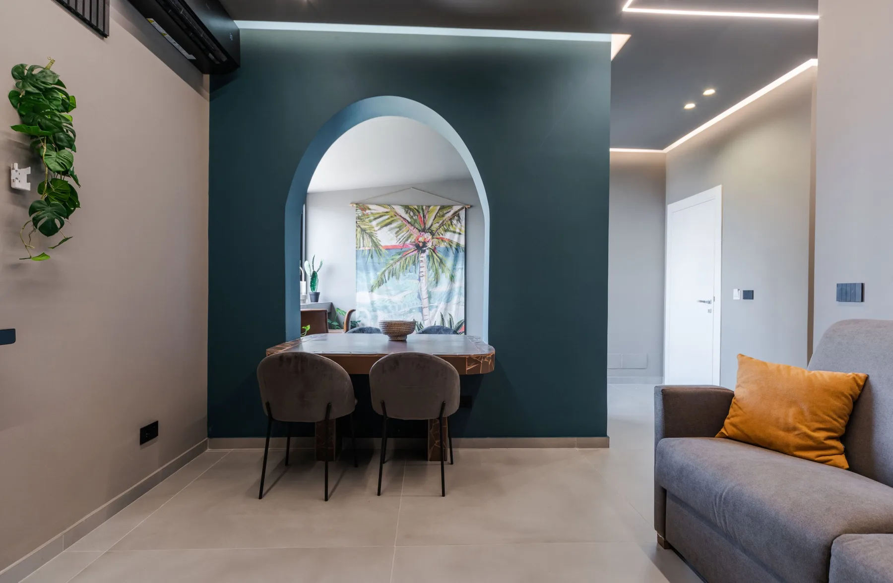A modern living and dining area with an arched opening and a gray sofa.