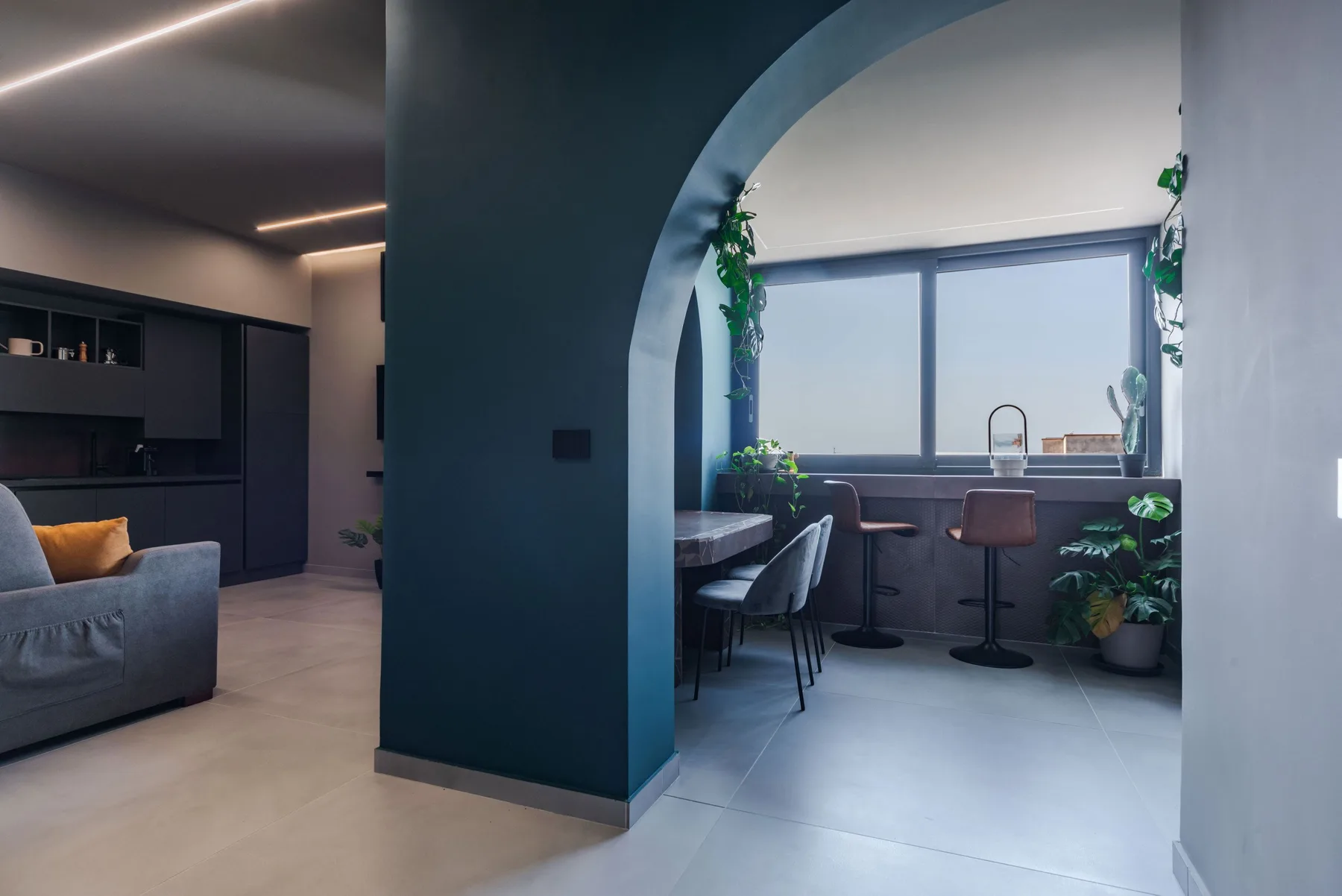 A modern living area opens onto a window-side counter with seating and plants.