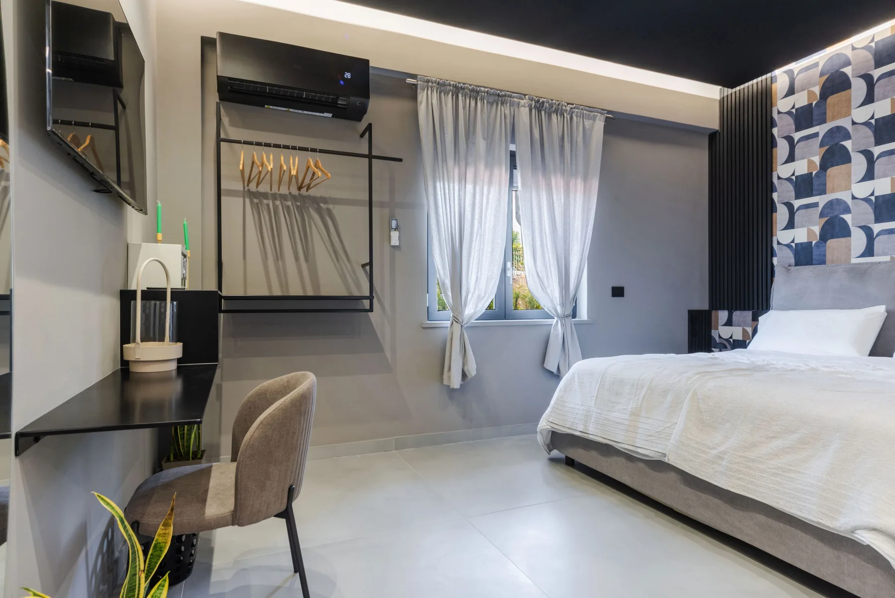 A bedroom with a bed, a desk, and a curtained window.