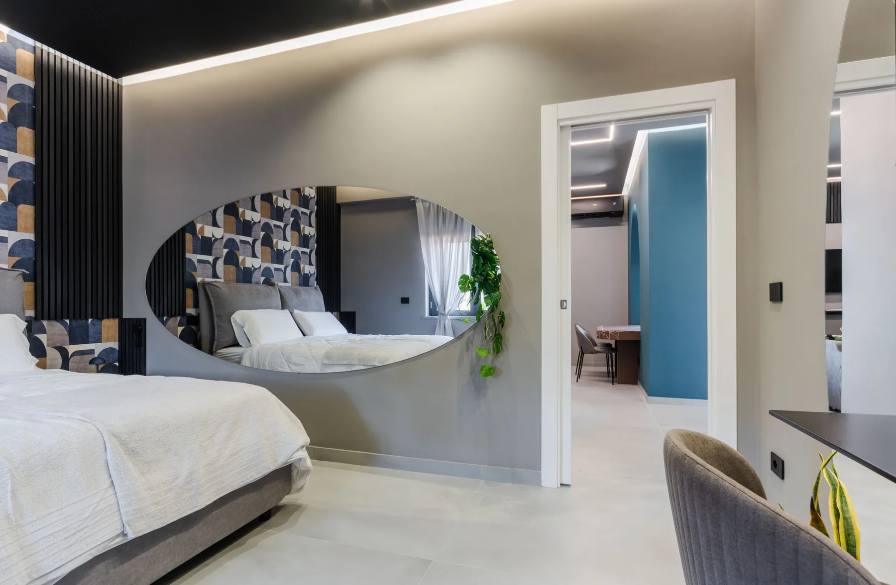 A bedroom with a bed, patterned wall panels, and an oval mirror.