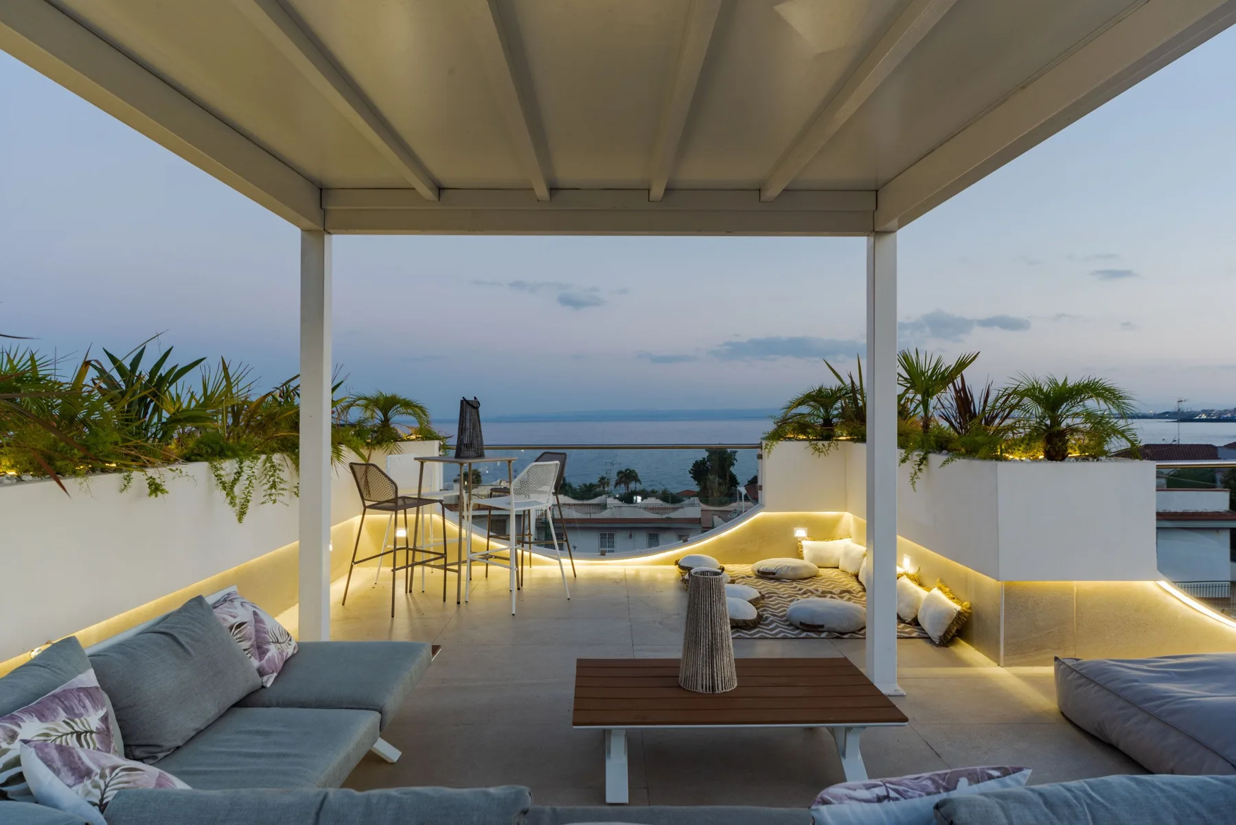 A covered rooftop terrace with outdoor seating and a view of the sea.