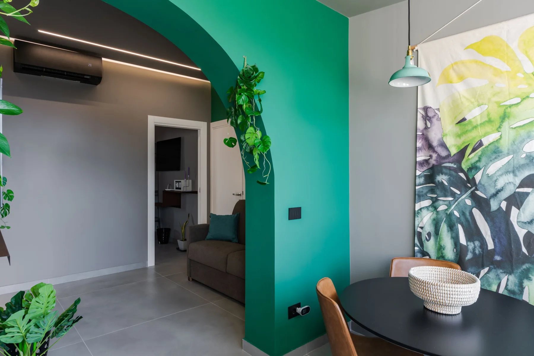 A dining area beside a teal wall and archway, with a leafy botanical artwork.