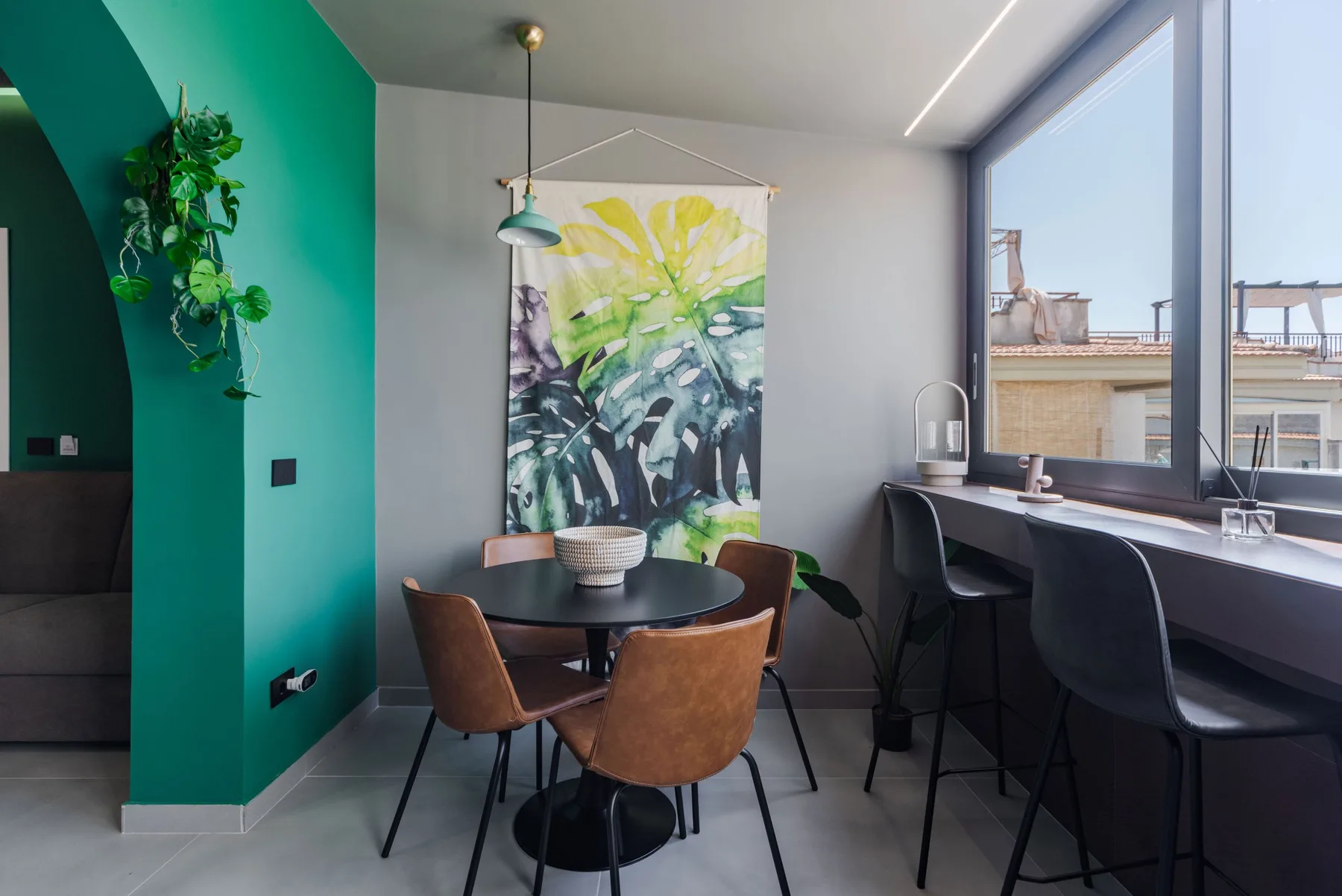 A dining area with a round table sits beside a large window and counter.