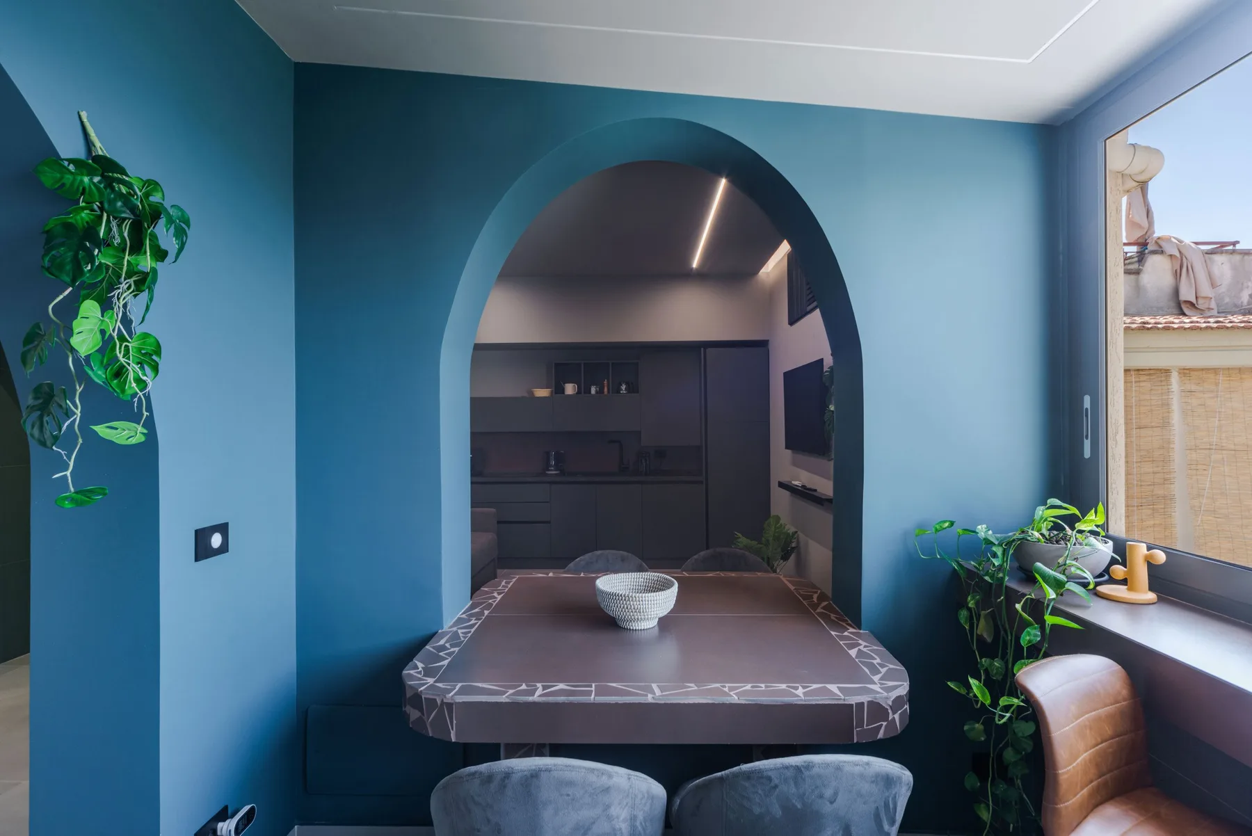 A dining area with a table beneath a large arch, opening onto a kitchen.