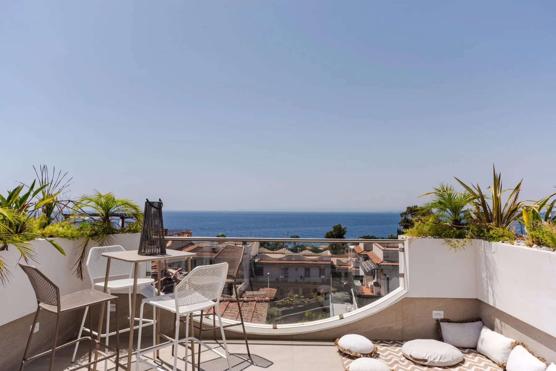 A rooftop terrace overlooks the sea, with outdoor seating and potted plants.