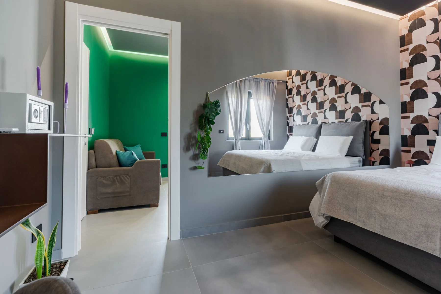 A bedroom with a bed and a large arched mirror reflecting the room.