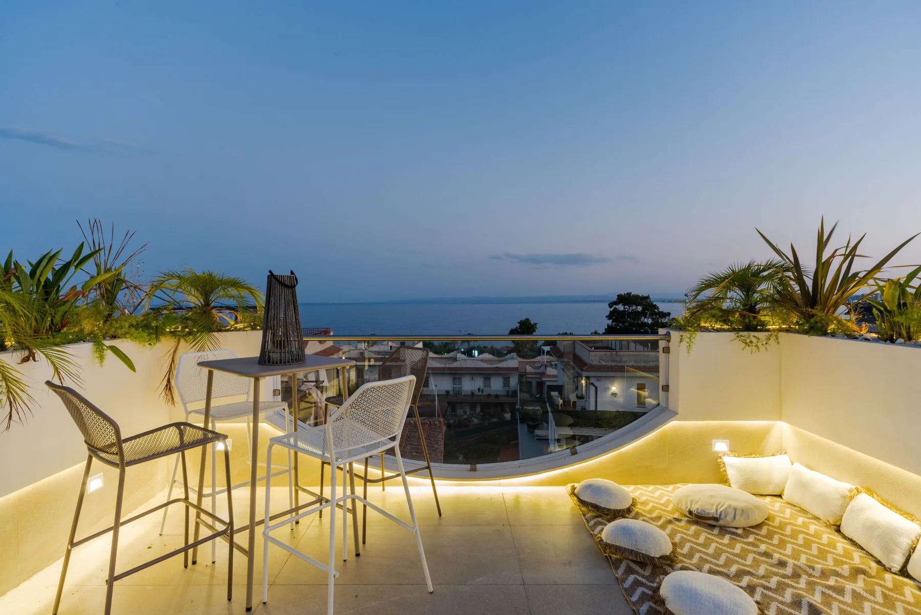 A rooftop terrace with seating and a cushioned lounge area overlooks the sea.