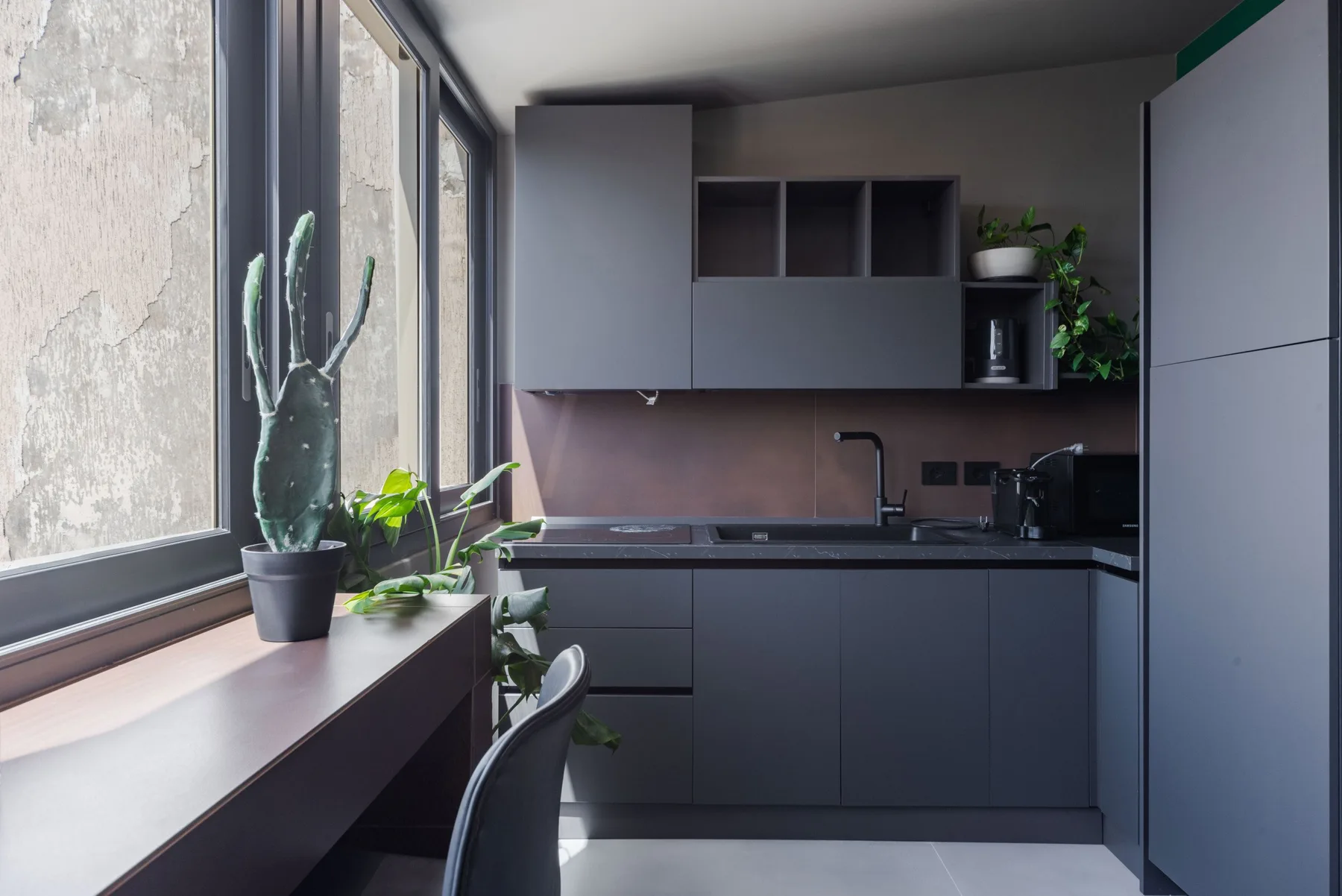 A modern kitchen with dark cabinetry, a sink, and plants by the window.