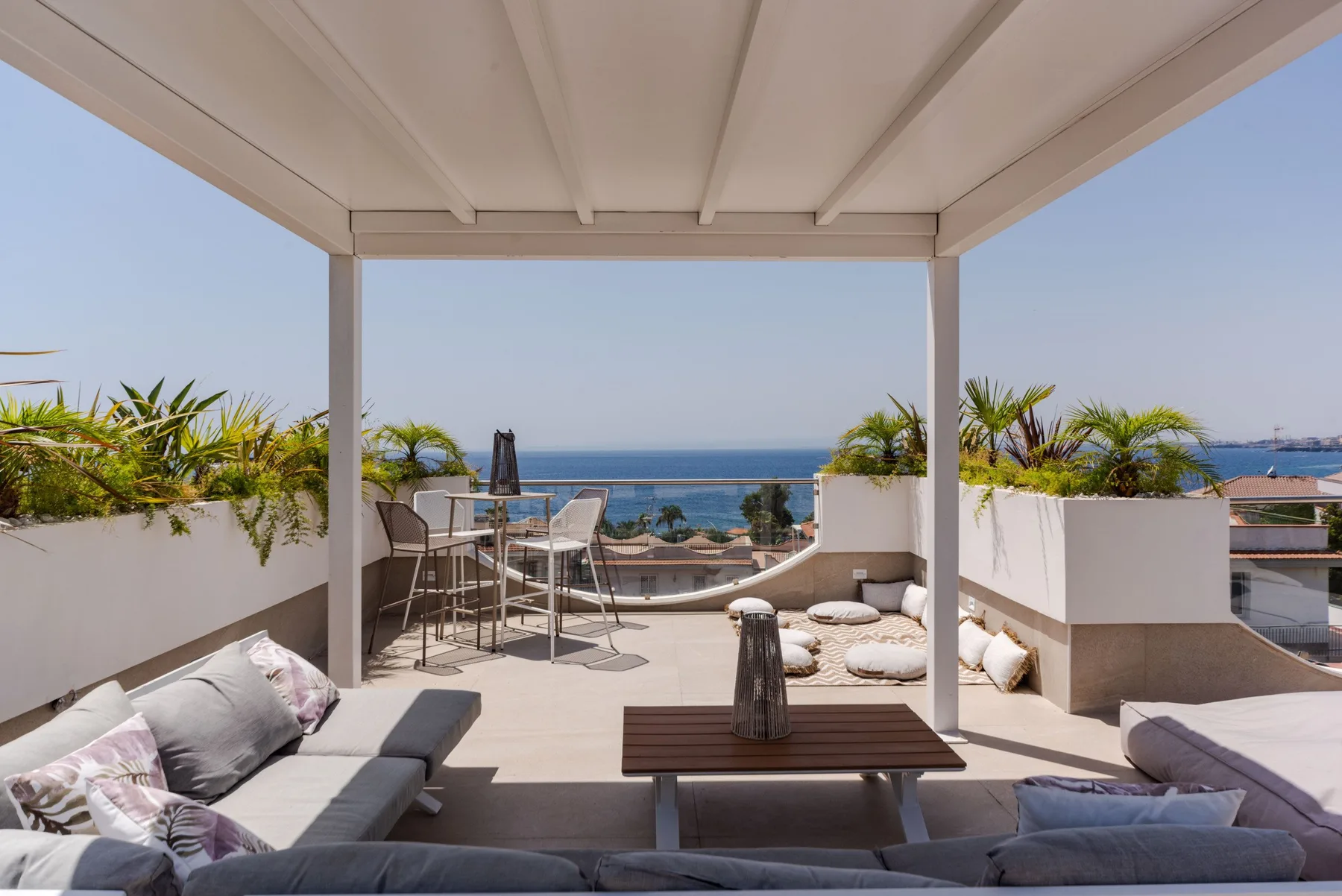 A furnished rooftop terrace overlooks the sea beneath a covered pergola.