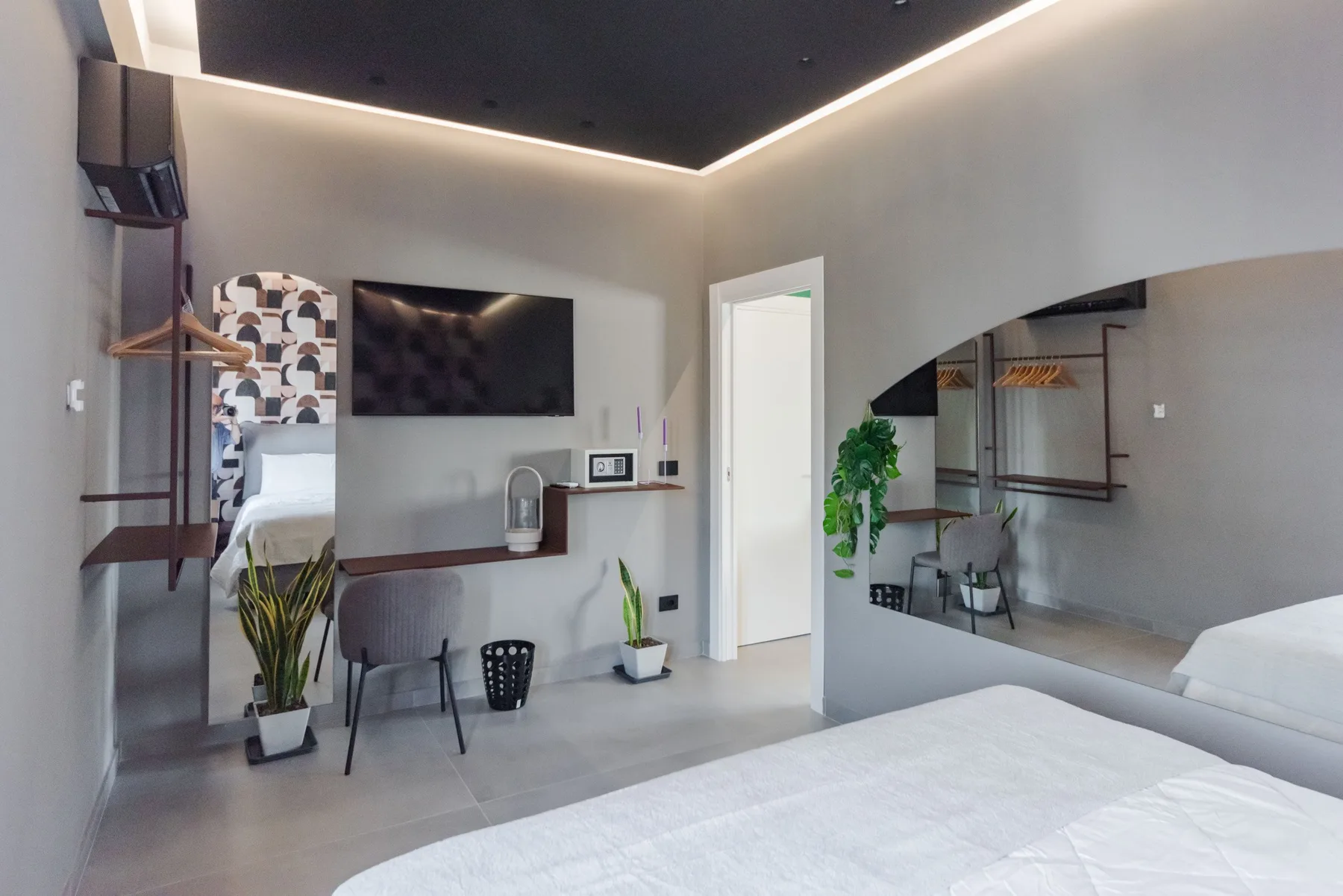 A modern bedroom with a bed, wall-mounted television, and a large mirror.
