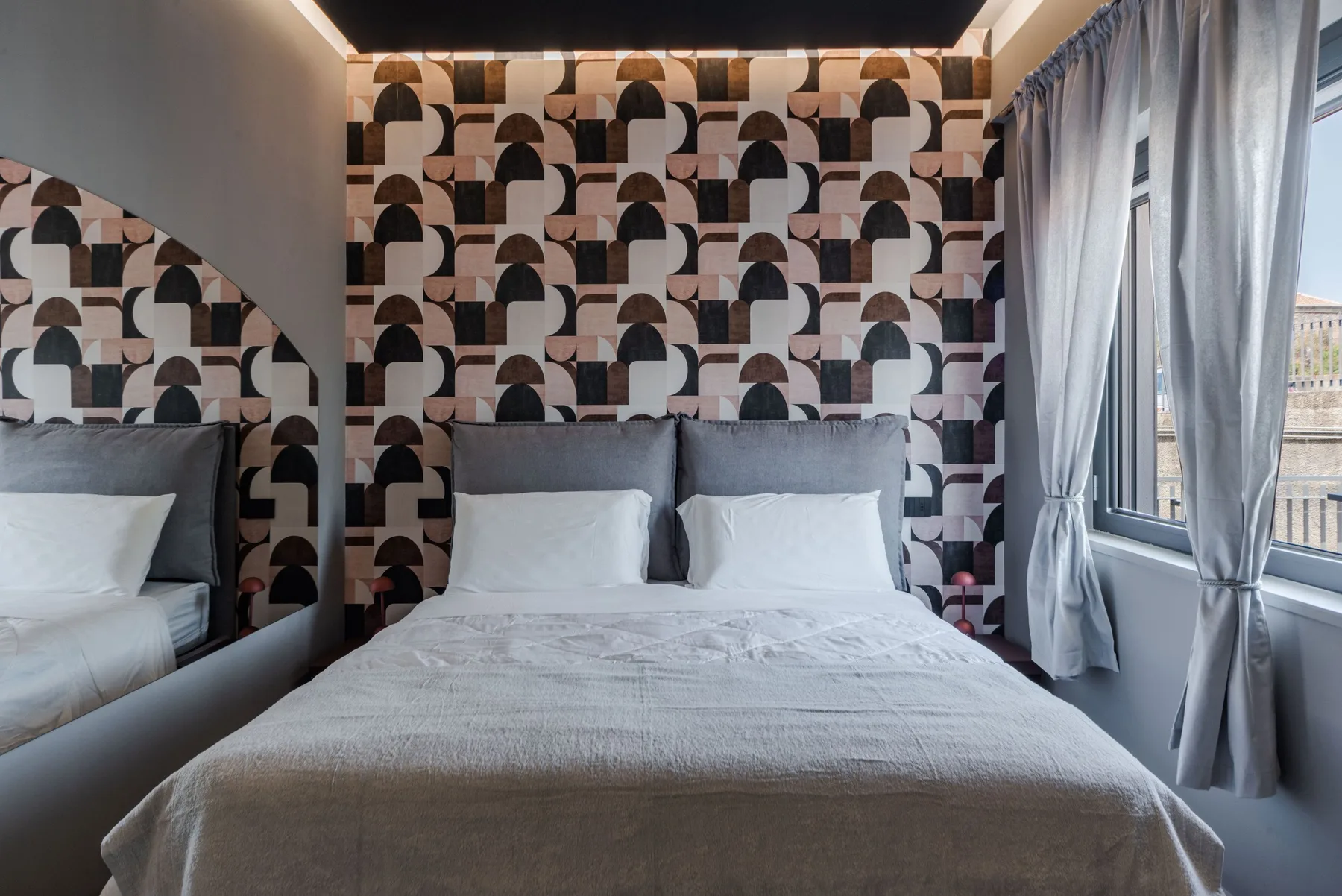 A bedroom with a neatly made bed against a patterned wall.