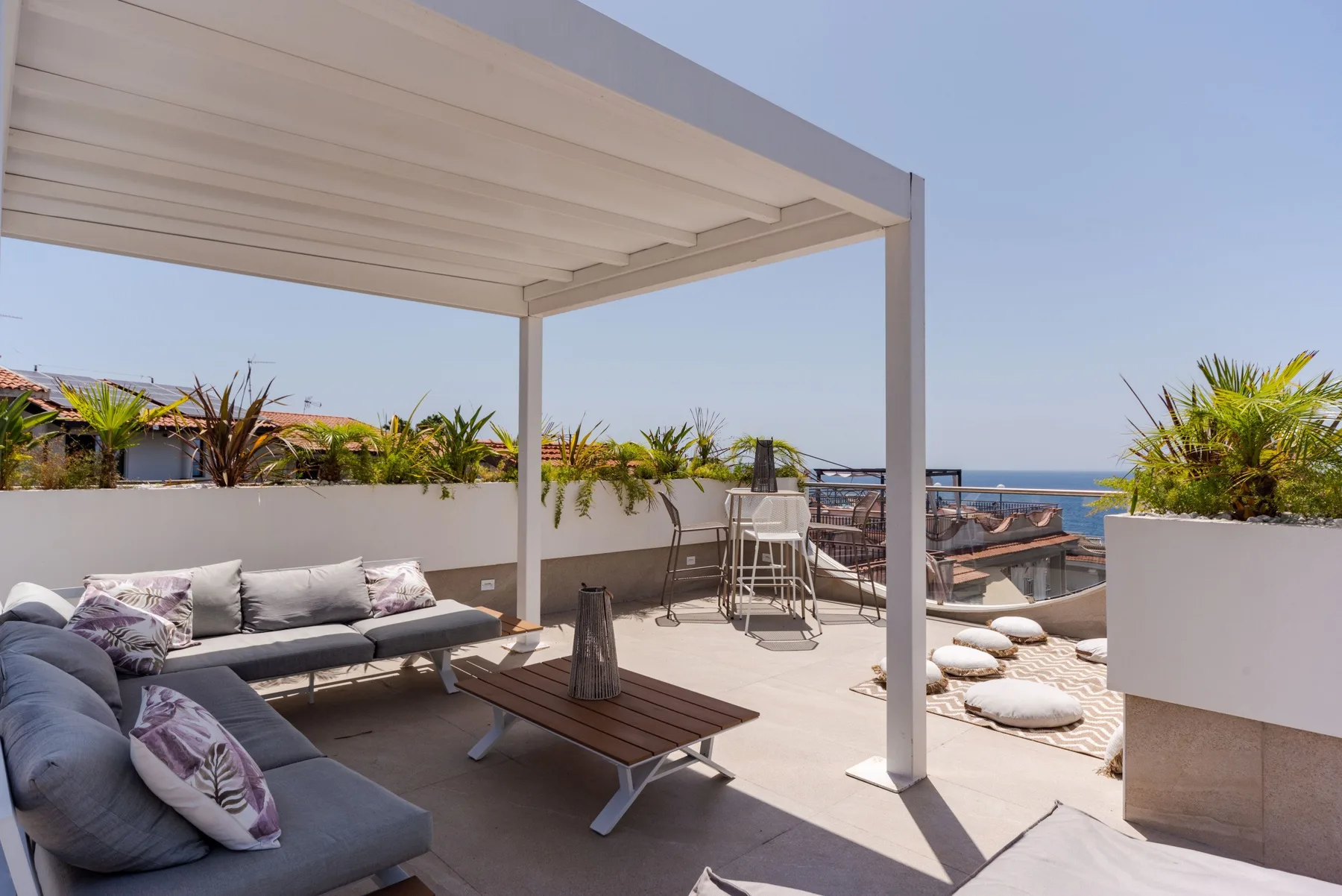 A covered outdoor seating area opens onto a terrace with views of the sea.