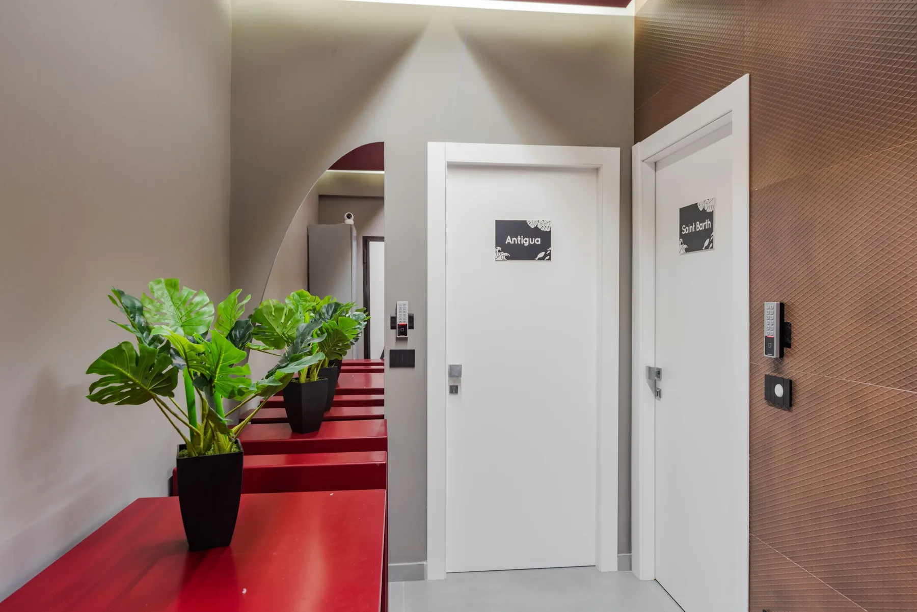 A hallway with white doors, red counters, and potted plants.
