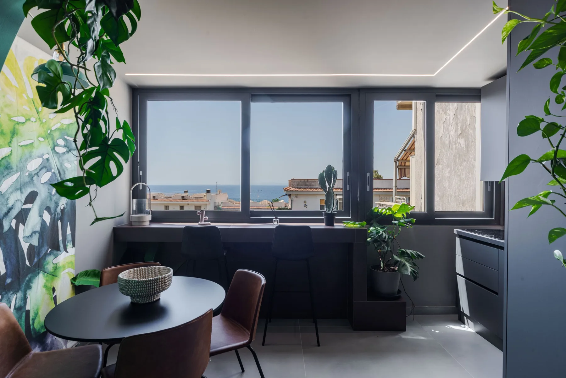 A bright kitchen with a counter and wide windows overlooking the sea.