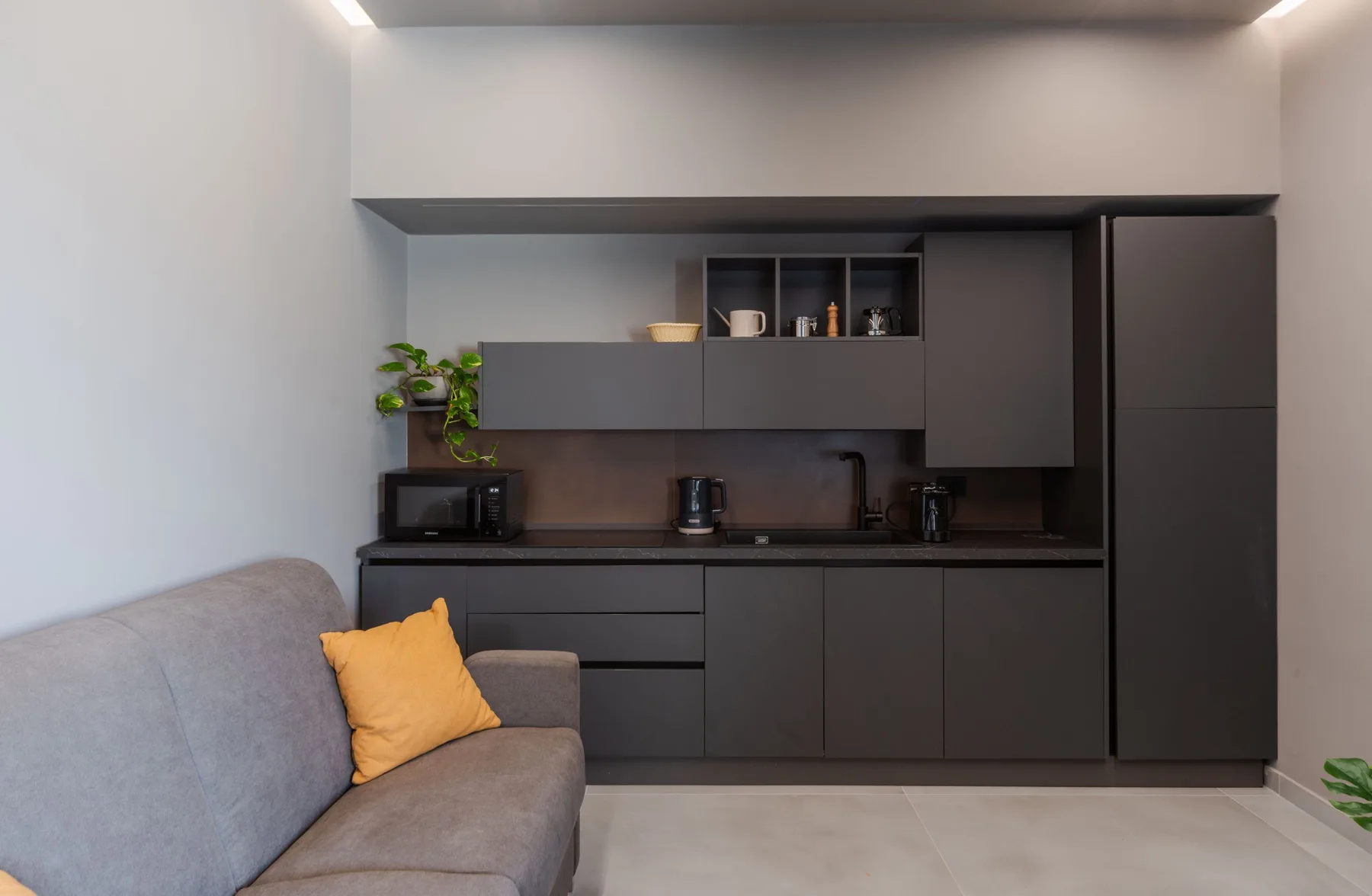 A compact living area with a gray sofa beside a dark kitchenette.