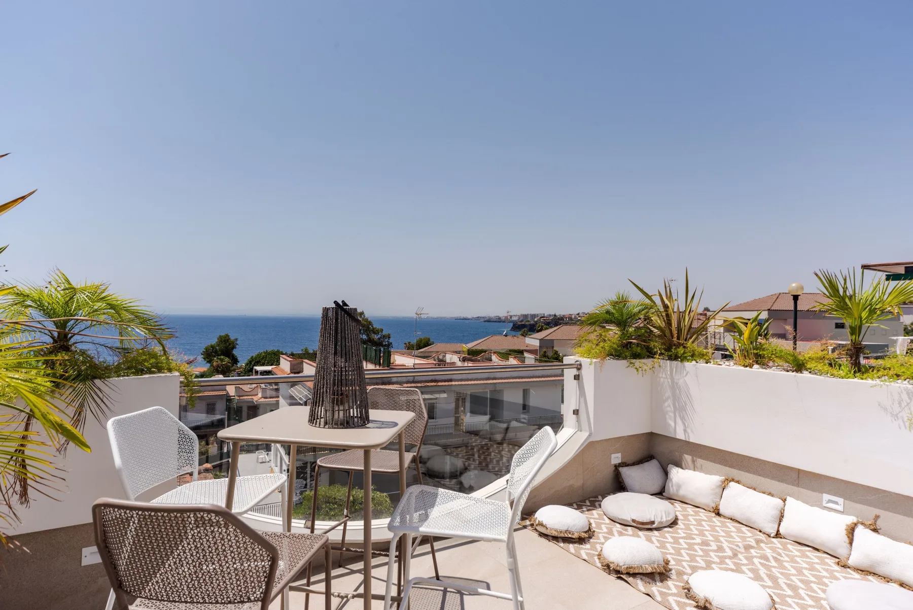 A rooftop terrace with outdoor seating and a cushioned lounge area overlooks the sea.