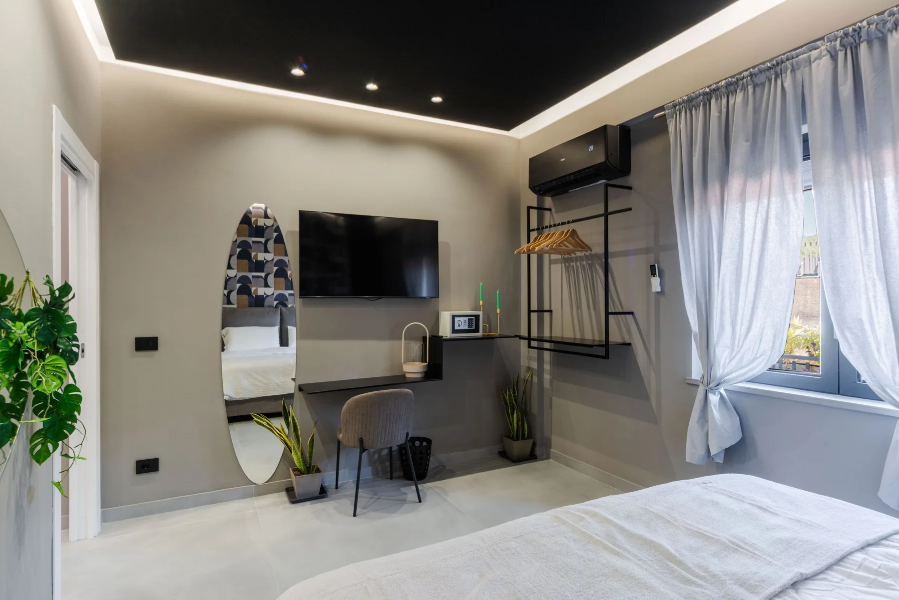 A bedroom with a wall-mounted television, desk, and a window with curtains.