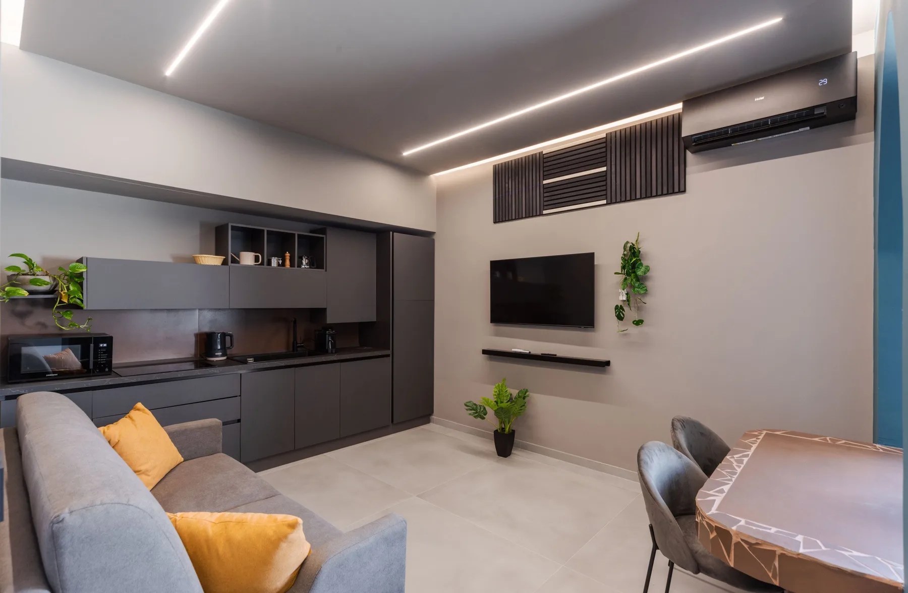 A modern living room with a wall-mounted television and built-in kitchenette.