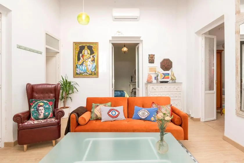 A bright living room with an orange sofa and a glass coffee table.