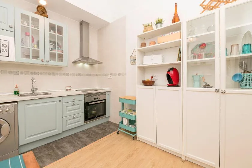 A bright kitchen with pale cabinets, open shelving, and a built-in oven.