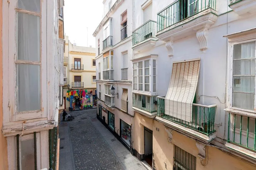 A narrow cobblestone street lined with white buildings and green balconies.